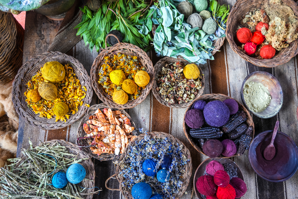 Hand-dyed wool balls in various shades of red, yellow, blue, and purple, created using traditional Peruvian techniques with natural plant and mineral pigments. These artisanal methods have been used for centuries in Andean textile production